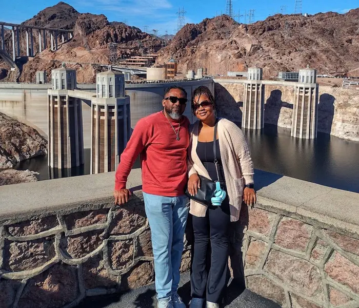 A couple poses in front of the Hoover Dam on a sunny day
